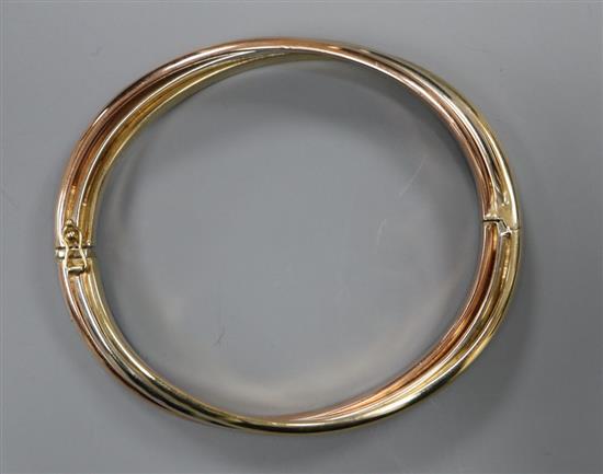 A 9ct three-colour gold bangle of oval, hollow, hinged design with overlapping bands, 18.1g